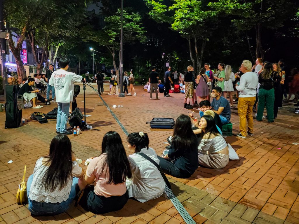 People sitting and listening to a singer at the Hongdae Playground